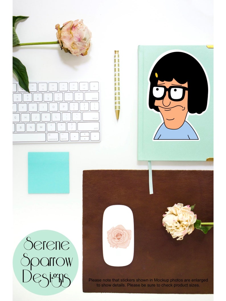 Puede incluir: Una pegatina con un personaje de dibujos animados con cabello negro, gafas y una camisa azul. La pegatina est&aacute; sobre un fondo verde claro. La pegatina est&aacute; sobre un escritorio con un teclado blanco, un bol&iacute;grafo dorado, una nota adhesiva azul claro y una alfombrilla de rat&oacute;n de cuero marr&oacute;n. Hay un rat&oacute;n blanco con una pegatina de rosa rosa en &eacute;l. Hay dos peon&iacute;as blancas en el escritorio.