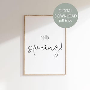 May include: A framed print with the words "hello spring!" in black script on a white background. The frame is a light wood color. A green circle in the upper right corner says "DIGITAL DOWNLOAD pdf & jpg".