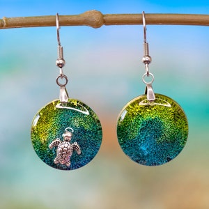 Könnte beinhalten: Ein Paar grüne und blaue Harzohrringe mit einem silbernen Schildkrötenanhänger an jedem Ohrring.