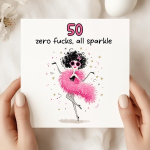 May include: A white greeting card with the text "50 zero fucks, all sparkle" and a cartoon illustration of a woman in a pink boa and sunglasses. The number 50 is in pink. The card is held by two hands.