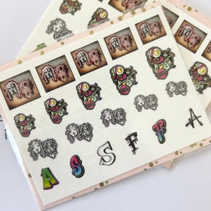 May include: A sheet of colorful nail stickers featuring various designs, including cartoon characters, letters, and abstract patterns. The stickers are on a white background.