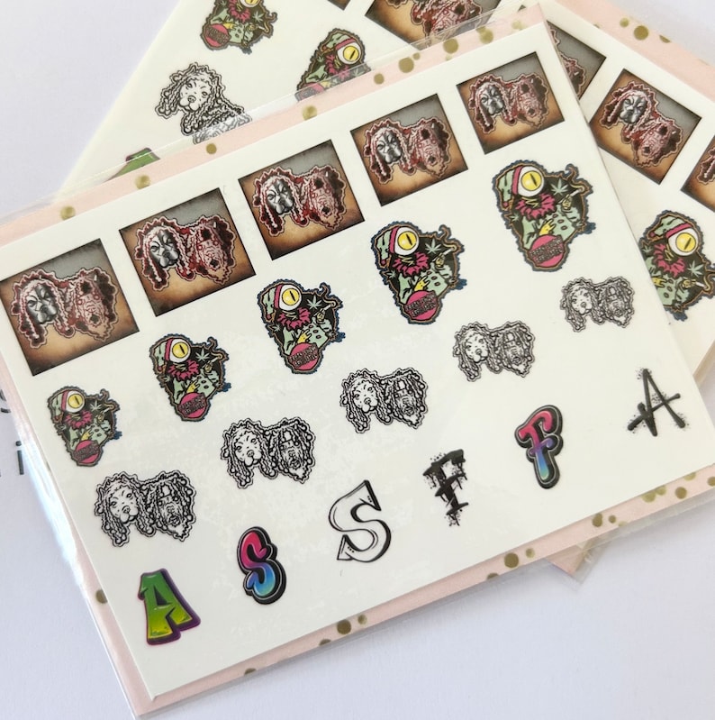 May include: A sheet of colorful nail stickers featuring various designs, including cartoon characters, letters, and abstract patterns. The stickers are on a white background.