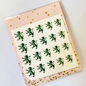 May include: A white sheet of paper with a repeating pattern of green lion silhouettes. The paper is on top of a pink sheet of paper with gold polka dots.