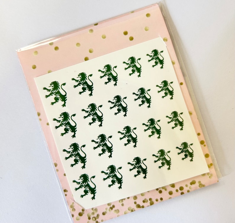 May include: A white sheet of paper with a repeating pattern of green lion silhouettes. The paper is on top of a pink sheet of paper with gold polka dots.