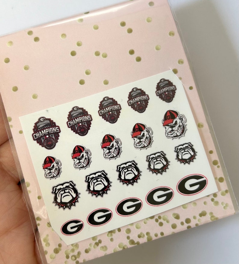 May include: A sheet of nail decals featuring the University of Georgia Bulldogs logo, including the team mascot, the words "Champions", and the team's "G" logo.