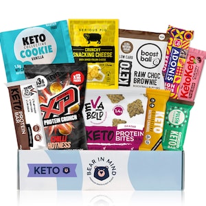 May include: A blue box with the words "Keto Bear in Mind" on the front. The box contains a variety of keto-friendly snacks, including protein bars, protein bites, and cheese snacks. The snacks are from different brands, including Keto Collective, Eva Bold, and Adonis.