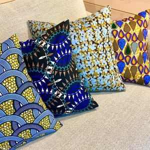 Peut inclure: Quatre coussins décoratifs aux motifs variés. Les coussins présentent des motifs floraux, géométriques et abstraits dans des tons de bleu, jaune et marron. Ils sont disposés sur un canapé de couleur neutre, ajoutant une touche décorative.