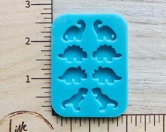May include: A blue silicone mold with six dinosaur shapes. The mold has two T-Rex dinosaurs, two Triceratops dinosaurs, and two long-necked dinosaurs.