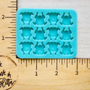 May include: A rectangular light blue silicone mold featuring twelve recessed cavities shaped like whole roasted turkeys. The mold is positioned against a wooden ruler, showing a width of approximately 3.25 inches and a height of 2.5 inches.