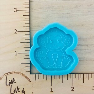 May include: A blue silicone mold of a cartoon monkey sitting with its legs crossed. The mold is about 2 inches wide and 2 inches tall.