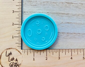 May include: A light blue silicone mold shaped like a pizza with a white outline of a pizza crust and white circles inside the pizza to represent cheese bubbles.