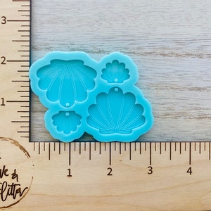 May include: A silicone mold with four different seashell shapes. The mold is light blue and has a smooth surface. The seashells are all different sizes and have a detailed design.