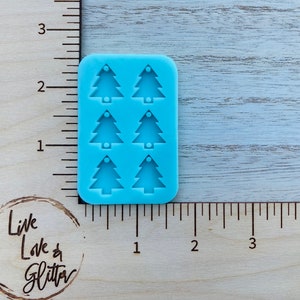 May include: A light blue silicone mold with six Christmas tree shapes. The mold is about 2 inches tall and 1 inch wide.