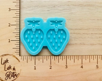May include: A light blue silicone mold for making two strawberry-shaped earrings. The mold is about 2 inches wide and 1 inch tall.