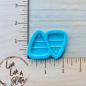 May include: A blue silicone mold for making two triangle-shaped earrings. The mold has three lines on each triangle and a small hole at the top of each triangle.