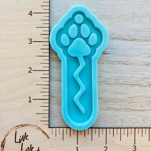 May include: A light blue silicone mold shaped like a paw print with a wavy line extending down from the paw print. The mold is approximately 4 inches tall and 1.5 inches wide.