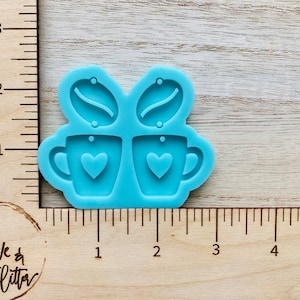 May include: A light blue silicone mold for making earrings. The mold features two coffee cups with hearts and two coffee beans.