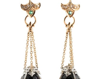 Peut inclure: Une paire de boucles d'oreilles pendantes dorées. Chaque boucle d'oreille présente un dessus floral avec de petits diamants et une émeraude, relié à une chaîne qui suspend une gemme noire à facettes enfermée dans un motif de filigrane argenté.