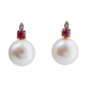 May include: A pair of pearl earrings. Each earring has a large, round, white pearl. Above the pearl is a small, square setting with a red gemstone and a diamond accent. The setting is gold-coloured.