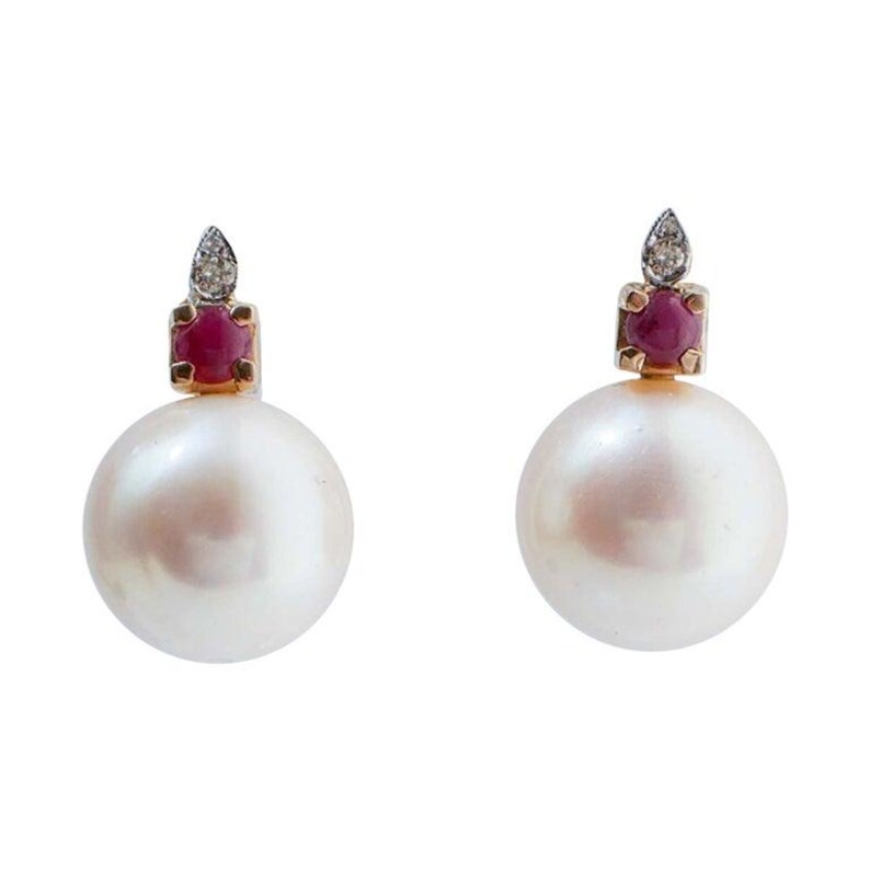 May include: A pair of pearl earrings. Each earring has a large, round, white pearl. Above the pearl is a small, square setting with a red gemstone and a diamond accent. The setting is gold-coloured.
