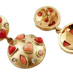 May include: A pair of gold earrings with red and pink coral stones and diamonds. The earrings are round and have a textured surface.