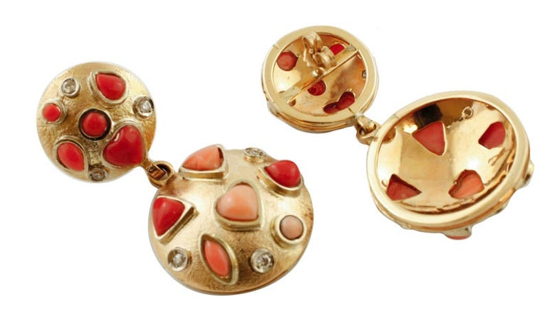 May include: A pair of gold earrings with red and pink coral stones and diamonds. The earrings are round and have a textured surface.