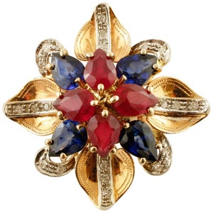 May include: A gold flower-shaped brooch with red and blue gemstones. The brooch is set with ruby and sapphire stones and has a diamond-encrusted border.