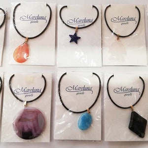 May include: A collection of necklaces with various pendant shapes, including a star, bear, and elephant. Each necklace features a black cord and a gold-colored clasp. The pendants are made of different materials and colors, and are displayed on white cards with the "Mareluna gioielli" logo.