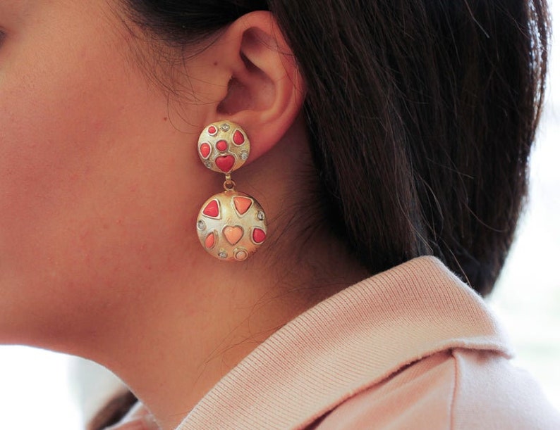May include: A pair of gold dangle earrings with pink and white heart-shaped stones. The earrings are made of metal and have a polished finish.