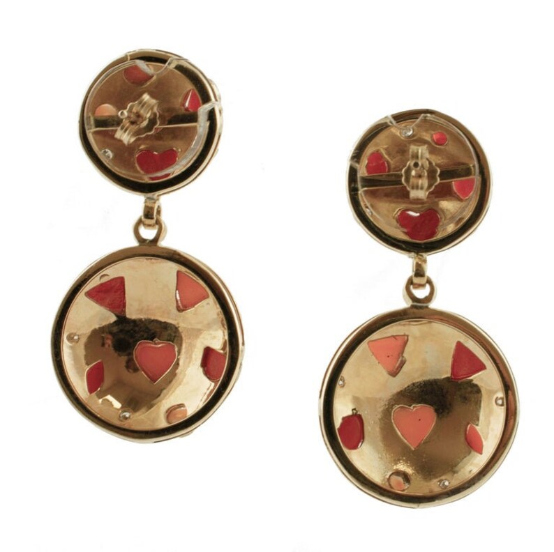 May include: Gold tone dangle earrings with two round discs. The larger disc has a textured surface with pink and red enamel hearts and geometric shapes. The smaller disc has a similar design with a red enamel heart.