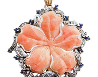 May include: A delicate coral flower pendant with a silver and diamond setting. The flower is surrounded by a halo of blue sapphires.