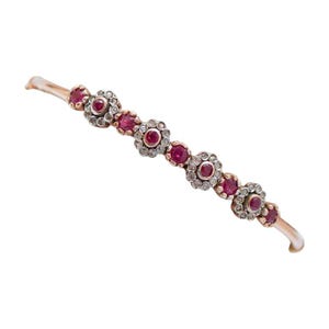 May include: A delicate bracelet featuring a series of ruby-colored gemstones set in floral designs. Each flower is surrounded by smaller, clear stones, creating a sparkling effect. The bracelet has a gold-toned metal band.