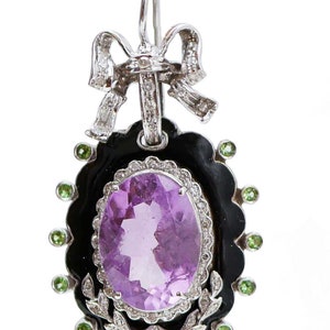 May include: An ornate earring featuring a large oval amethyst gemstone set in a black frame, surrounded by green accents. The earring has a silver bow at the top and a decorative leaf design at the bottom. The earring is designed for pierced ears.