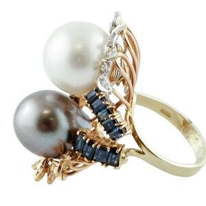 May include: A gold ring featuring a white and black pearl design. The ring is set with blue sapphires and diamonds.