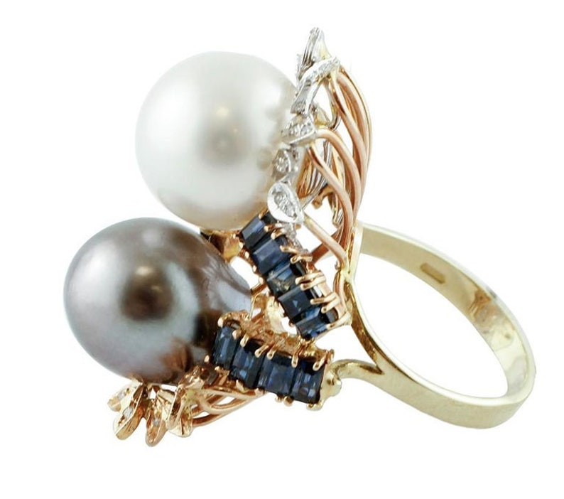May include: A gold ring featuring a white and black pearl design. The ring is set with blue sapphires and diamonds.