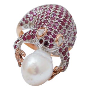 May include: A unique ring featuring a stylized octopus design. The octopus is encrusted with small, round, deep pink gemstones and holds a large, white, pear-shaped pearl. The ring has a gold band and accents.