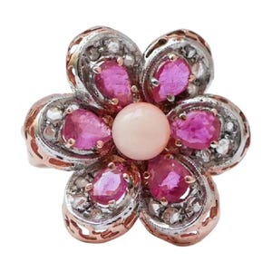 May include: A flower-shaped ring featuring a central round pale pink stone surrounded by five pear-shaped vibrant pink rubies. The petals are crafted from silver-toned metal with intricate filigree detailing and rose gold-toned edges.