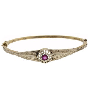 Puede incluir: Un brazalete de oro con un diseño intrincado y una piedra preciosa rosa en el centro.