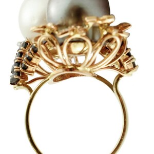 May include: A gold ring featuring a black and white pearl setting. The ring is embellished with black gemstones.