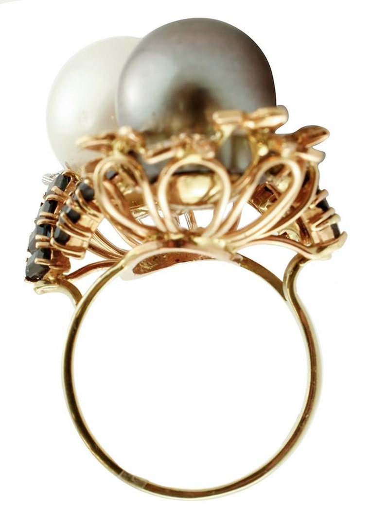May include: A gold ring featuring a black and white pearl setting. The ring is embellished with black gemstones.