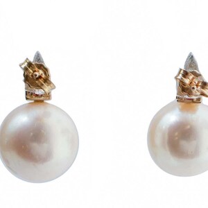 May include: A pair of pearl earrings. Each earring has a large, round, lustrous pearl. The posts and clasps are gold-toned, with a silver accent. The earrings are set against a white background.