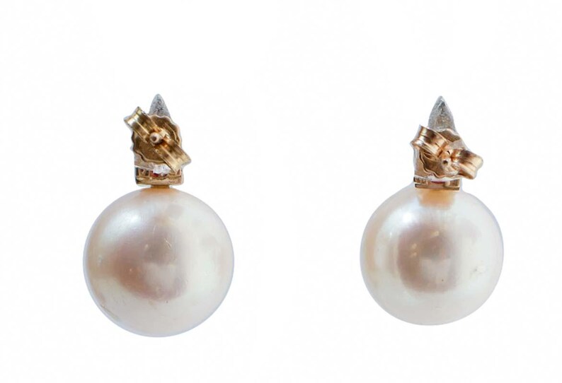 May include: A pair of pearl earrings. Each earring has a large, round, lustrous pearl. The posts and clasps are gold-toned, with a silver accent. The earrings are set against a white background.