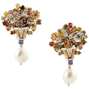 May include: A pair of gold earrings with a floral design. Each earring features a small flower pot with a pearl drop hanging from it. The flower pots are adorned with colorful gemstones and diamonds.