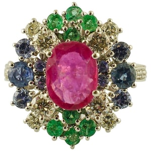 Pode incluir: Um anel com um grande rubi oval rosa cercado por pequenas esmeraldas verdes, safiras azuis e diamantes brancos.