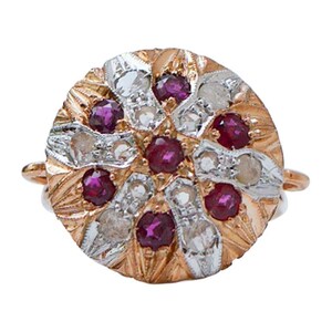 Pode incluir: Um anel circular com um rubi central rodeado por pétalas alternadas de ouro rosa e metal prateado. O design inclui seis rubis adicionais e seis pedras claras cravadas nos segmentos metálicos texturizados e radiantes.
