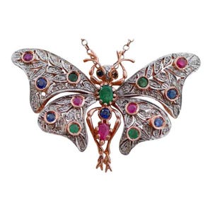 Puede incluir: Un collar con colgante de mariposa con un diseño detallado. Las alas son plateadas con piedras transparentes y gemas de colores. El cuerpo y las antenas son dorados. Las gemas son rojas, verdes y azules.