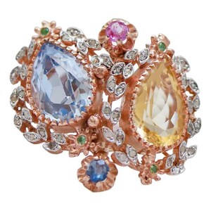 Op de afbeelding: Een roségouden ring met een grote peervormige lichtblauwe edelsteen en een peervormige gele edelsteen. De ring is versierd met kleine heldere steentjes, kleine groene accenten, een ronde roze steen en een kleine ronde blauwe steen in bloemmotief.