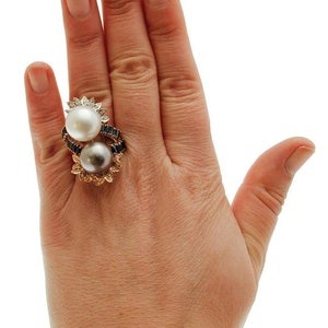 May include: A gold ring featuring two pearls, one white and one grey, set in a floral design with black diamonds.