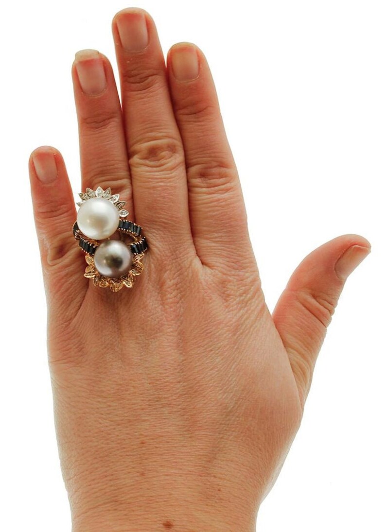 May include: A gold ring featuring two pearls, one white and one grey, set in a floral design with black diamonds.