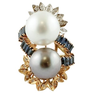 May include: A gold brooch featuring two pearls, one white and one grey, encircled by blue sapphires and diamonds.